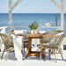 Grey rattan outdoor dining side chairs with a matching round wooden dining table overlooking the ocean.