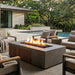 Outdoor patio with rectangular concrete fire pit with an element of teak slats, chairs, and pool area