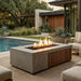 Outdoor patio with rectangular concrete fire pit with an element of teak slats, pool, and modern house