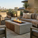 Outdoor patio with rectangular concrete fire pit with an element of teak slats, chairs, and couches on a sunny day.