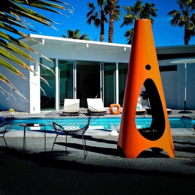 Orange cone-shaped outdoor metal fire pit placed beside the pool in front of a small white house with glass wall