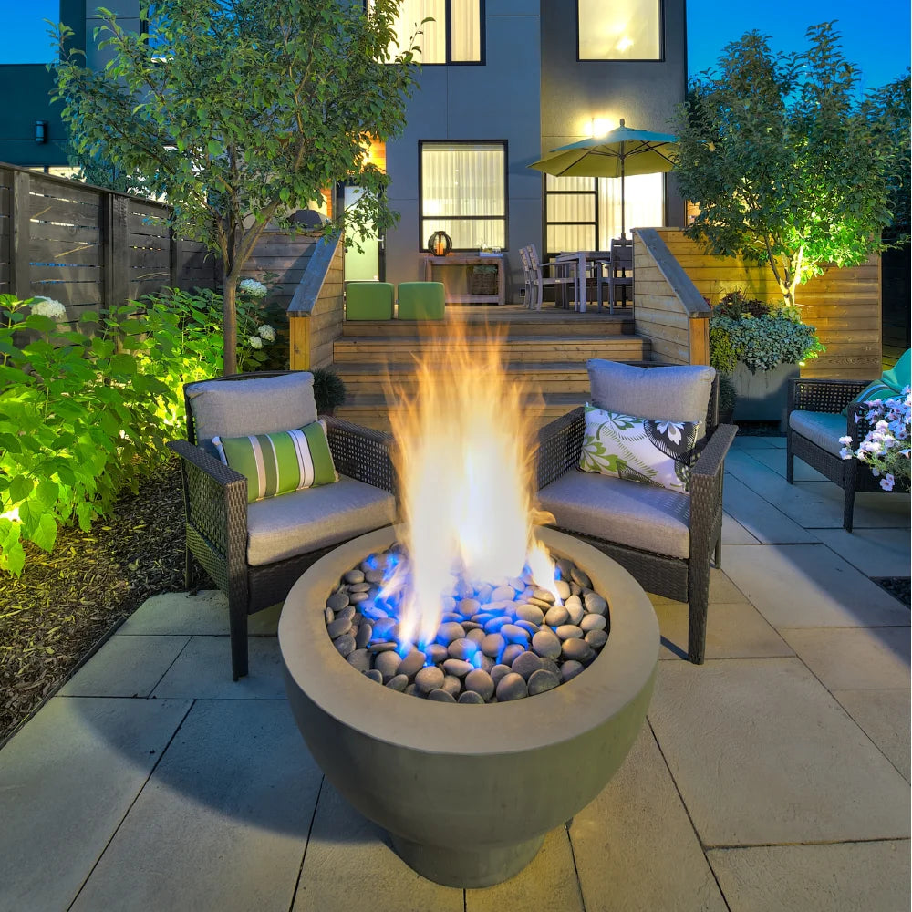 Modern patio with gray fire pit bowl, two gray lounge chairs, and garden setting at night.
