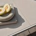 Close up view of white ceramic outdoor dining table with a book and a sliced fruit on top.