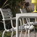 White outdoor dining table and two white dining chairs set on a patio  with tall grasses in the background.