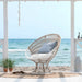 White rattan outdoor sun chair with white cushions in a beachside setting overlooking the ocean.