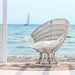 White rattan outdoor sun chair with white cushions in a beachside setting overlooking the ocean.