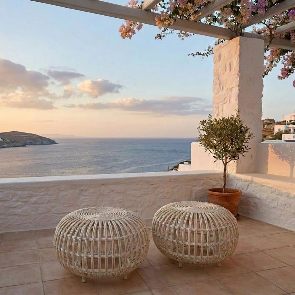 Natural wicker outdoor ottomans in a light tan finish with open woven frames on a seaside terrace.