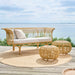Natural wicker outdoor ottomans with a matching sofa featuring white cushions on a seaside deck.