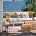 Natural wicker outdoor ottomans beside a matching wicker sofa with white cushions overlooking the water.