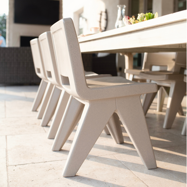 An outdoor dining set up on a patio with several light gray outdoor dining chairs set around a wooden dining table