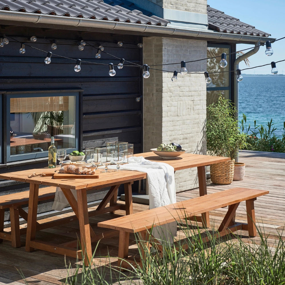Natural wooden outdoor bench beside a matching picnic table set on a deck overlooking the water.
