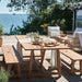 Natural wooden outdoor benches with a matching dining table set on a waterfront deck beneath string lights.