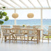 Natural wooden outdoor dining table with matching wicker dining chairs overlooking the ocean.