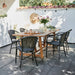 Natural wooden outdoor dining table with matching black rattan dining chairs on a tiled patio.