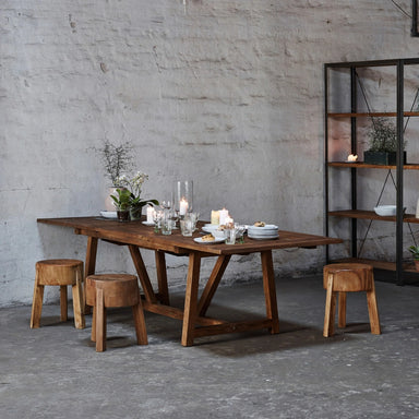 Natural teak outdoor dining table with matching wooden stools styled with candles and glassware.