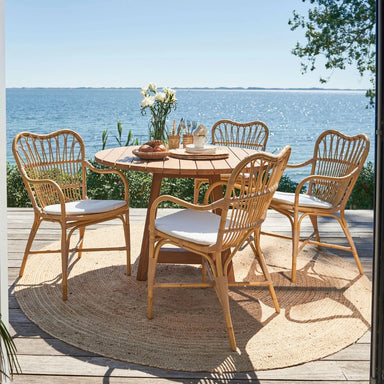 Natural wooden outdoor round dining table with four matching wicker dining chairs overlooking the ocean.