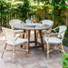 Natural wooden outdoor round dining table with four matching white wicker dining chairs on a brick patio.