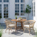 Natural wooden outdoor round dining table surrounded by four wicker dining chairs with white cushions. 