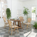 Natural wooden outdoor round dining table with matching wicker dining chairs on a checkered floor.