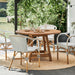 Natural wooden outdoor round dining table with matching wicker dining chairs on a jute rug.