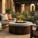 Outdoor patio with round concrete outdoor fire pit table, seating area, and garden plants.
