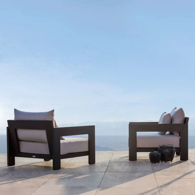 Two modern outdoor lounge chairs with gray cushions on a patio with a scenic view under clear blue sky.