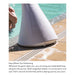 A white cone-shaped pool hoop holder positioned next to a swimming pool, with a person's hand visible at the top left. The image includes descriptive text at the bottom about easy wheel-out positioning.