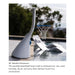 A white poolside basketball hoop mounted on a swimming pool deck, with a blue rim and white net. The background shows a blurred outdoor poolside setting with trees and water.