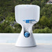 A white outdoor portable basketball hoop with a blue rim and a blue ball, set on a patio with a green forest background.