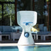 A white and blue LEGGE poolside basketball hoop with a white net, set on a pool deck in front of a modern patio lounge with blue cushions.