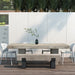 Rectangular concrete dining table and concrete outdoor bench with black steel legs, and four white chairs on a wooden deck patio with white wall