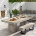 White patio with rectangular concrete dining table and concrete outdoor bench with black metal legs, plants and corner seating with gray cushions and throw pillows