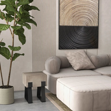 Modern living room with small concrete outdoor side table or stool with black metal legs, potted plant, gray modular sofa with pillows, and circular textured wall art