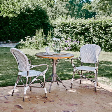 Natural rattan outdoor dining armchairs with a matching round wooden dining table in a lush garden.