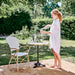 White wicker outdoor armchair beside a bistro table with a person pouring water on a garden patio.
