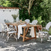 Outdoor dining with white rattan dining chairs and a wooden dining table surrounded with greenery.