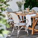 White wicker outdoor dining armchairs and wooden dining table set for outdoor dining.