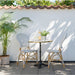 Natural rattan outdoor dining side chair beside a matching round bistro table on a patio.