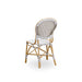 angled view of a natural rattan outdoor dining side chair with a cappuccino and white patterned woven back.