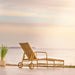 Natural rattan outdoor sun lounger with white cushions viewed from the angled rear overlooking the sea.