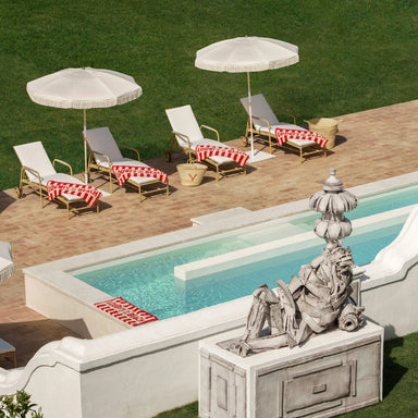 Natural rattan outdoor sun loungers with rear wheels, red and white striped towel beside a swimming pool.