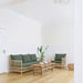 Natural teak outdoor coffee table beside a matching rattan sofa and lounge chair with green cushions.