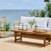 Natural teak outdoor coffee table with matching rattan sofa featuring white cushions on a seaside patio.