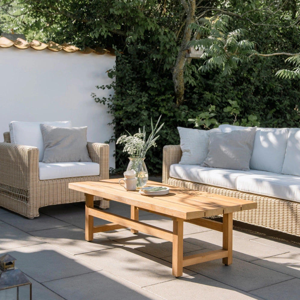 Natural wooden outdoor coffee table with matching wicker sofa and lounge chair featuring white cushions.