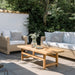 Natural wooden outdoor coffee table with matching wicker sofa and lounge chair featuring white cushions.