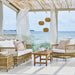 Natural teak outdoor coffee table with matching rattan sofa and lounge chair featuring white cushions.