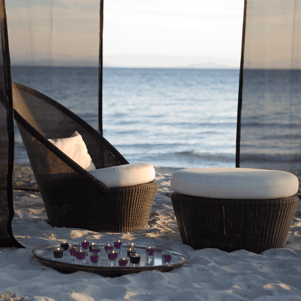 Boxhill's Kingston Sunchair Lounge with Wheels lifestyle image at the beach sand with Kingston Outdoor Footstool | Side Table and candle lights at the side