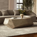 Modern living room with a curved beige sofa, geometric concrete coffee table, beige vase with branches, and a textured rug.