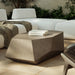 Gray concrete outdoor coffee table with geometric shape, white sectional sofa on a tiled patio surrounded by greenery