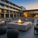 Outdoor lounge area with a 72" square concrete fire pit table in front of a modern building
